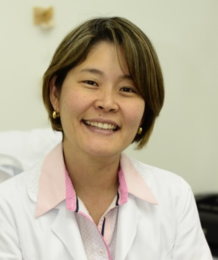 Dra. Eneida Mari Yoshida sorrindo, de jaleco, no consultório